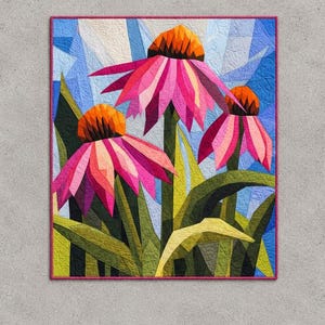 May include: A rectangular fabric quilt featuring a geometric pieced design of three coneflower blossoms with vibrant pink petals and orange centers, set against a background of blue sky and green foliage, finished with a thin pink border.