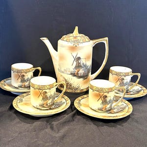 May include: A vintage tea set featuring a teapot and four teacups with saucers. The set is painted with a windmill scene in shades of beige, brown, and gold. The teapot has a gold handle and spout, and the cups have gold rims.