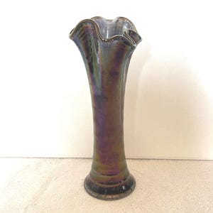May include: A tall, iridescent glass vase with a ruffled rim. The vase has a slender, elongated body and a flared base. The colors shift from purple to gold and green, creating a shimmering effect. The vase is likely for decorative purposes.
