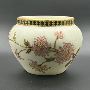 May include: A round, off-white ceramic bowl featuring a hand-painted design of pink chrysanthemums with green leaves and gold outlines. The rim is decorated with a band of dark green enamel ovals framed by gold, creating a detailed border.