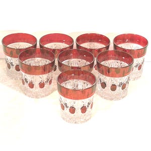 May include: Set of eight clear crystal glasses with a red rim and red dot accents. The glasses have a cut crystal design and are arranged in a circular pattern. The glassware is suitable for serving beverages.