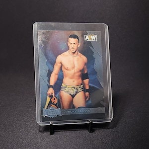 Könnte beinhalten: Sammelkarte mit Ricky Starks, einem professionellen Wrestler, in einer Schutzhülle. Die Karte hat ein metallisches Finish und zeigt das AEW-Logo. Starks ist ohne Hemd und hält einen Championgürtel.