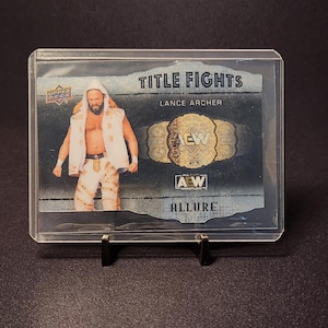 May include: A trading card featuring Lance Archer from the "Title Fights" series. The card displays Archer in wrestling attire, the AEW championship belt, and the "Allure" logo. The card is encased in a clear protective holder.