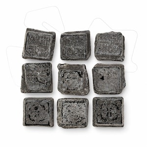 May include: A collection of nine square, dark gray, textured blocks arranged in a three-by-three grid. Each block features a distinct, embossed geometric or symbolic pattern on its top surface, with rough, uneven edges and a weathered, matte finish.