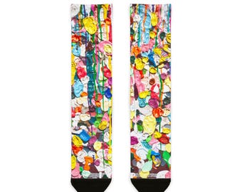 May include: A pair of colorful socks with a vibrant abstract design. The socks feature a pattern of multi-colored paint splotches and drips in shades of yellow, blue, pink, green, and red. The socks have black toes and heels.