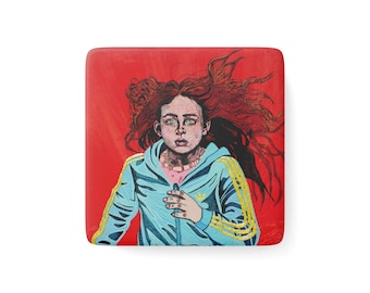 May include: A square coaster featuring a graphic illustration of a person with long, flowing red hair and wide green eyes. The person wears a light blue zip-up hoodie with yellow stripes on the sleeves, set against a solid, vibrant red background.