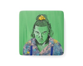 May include: A square coaster featuring a green-toned illustration of a person with a yellow hair scrunchie in a top knot, a nosebleed, and a patterned shirt with blue straps against a solid green background with visible brushstroke textures.