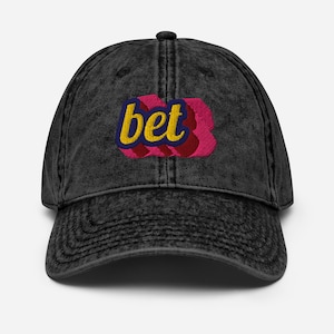 May include: A black, vintage-style baseball cap with the word "bet" embroidered on the front. The word is in yellow, outlined in blue, and set against a pink and red background.