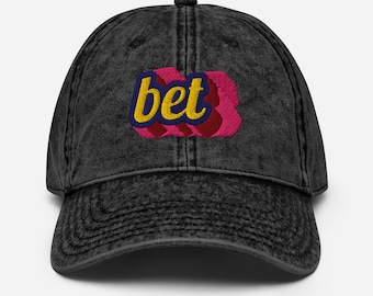May include: A black, vintage-style baseball cap with the word "bet" embroidered on the front. The word is in yellow, outlined in blue, and set against a pink and red background.