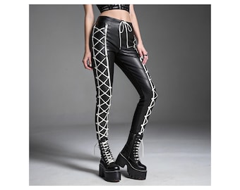 May include: Black faux leather pants with white crisscross lacing details down the sides. The pants have a zipper closure and a drawstring waist. The model is wearing black platform boots with white laces. The pants are a stylish, edgy fashion item.