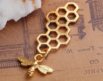 Puede incluir: Encanto dorado con un diseño de panal de abejas y un pequeño colgante de abeja. El encanto está hecho de metal y tiene un acabado brillante.