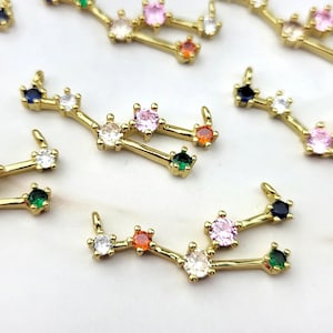 May include: A set of gold-toned zodiac constellation charms with colorful crystal accents. Each charm features a different constellation design with a variety of colored crystals, including pink, blue, green, and orange.