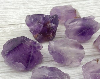 May include: A collection of eight amethyst crystals, each with a unique shape and size. The crystals are a deep purple color and have a natural, rough texture.