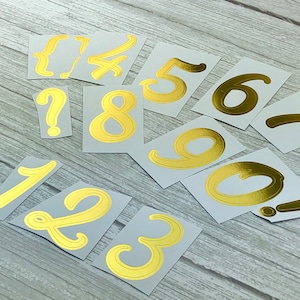 May include: Gold numbers and an exclamation mark on white cardstock. The numbers are 1, 2, 3, 4, 5, 6, 7, 8, 9, 0, and a question mark.