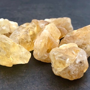 May include: A group of six raw, unpolished, yellow citrine crystals. The crystals are various sizes and shapes, with some having a more translucent appearance than others.