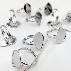 Op de afbeelding: Tien zilverkleurige ringen met een traanvormige bezel voor het instellen van een steen of cabochon. De ringen zijn verstelbaar en hebben een gladde, gepolijste afwerking.