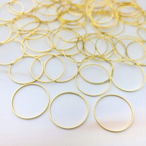 Op de afbeelding: Een verzameling goudkleurige metalen cirkelringen, mogelijk voor het maken van sieraden of knutselen. De ringen zijn gerangschikt op een wit oppervlak, met veel op de achtergrond en een paar op de voorgrond.