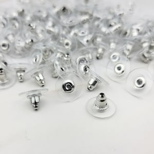 May include: A close-up of a pile of clear plastic earring backs with silver metal posts. The backs are round and have a small hole in the center. The posts are threaded and have a small ball on the end.