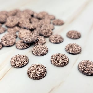 May include: A pile of rose gold glitter round cabochons, perfect for crafting and jewelry making.