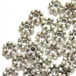 May include: A pile of silver metal bead caps with a flower-shaped design. Each cap has a small hole in the center.