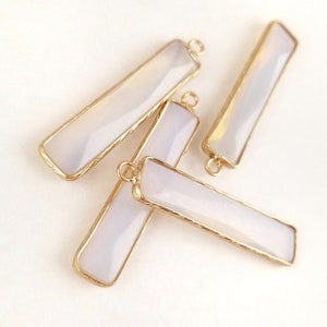 May include: Four white agate bar pendants with gold-toned metal frames and jump rings. The pendants are rectangular and have a slightly textured surface.