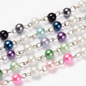 May include: Close-up of several strands of colorful faux pearl beads. The beads are connected by silver-colored chain links. The pearls are in various colors, including white, black, blue, purple, green, and pink. The background is white.