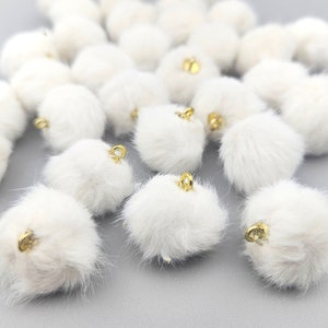May include: A collection of white fluffy pom poms with gold metal loops. The pom poms are arranged in a random pattern on a white surface.