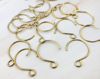 May include: A group of gold-toned metal earring hooks. The hooks are all the same size and shape, and they are arranged in a random pattern.
