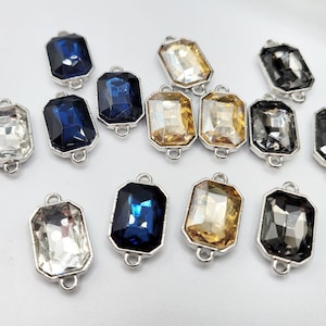 Puede incluir: Surtido de gemas de vidrio transparente, dorado y azul con engastes plateados. Las gemas son rectangulares y tienen un diseño facetado.