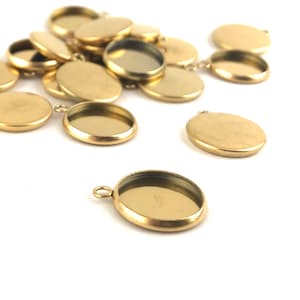 May include: A group of gold-toned metal pendant trays with a round shape and a smooth surface. The trays have a small loop at the top for attaching to a chain or cord.