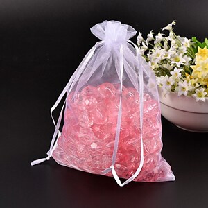 May include: White organza gift bag with a drawstring closure, filled with pink crystal-like beads.