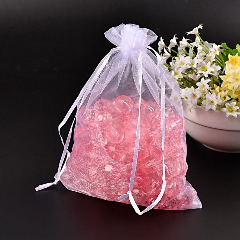 May include: White organza gift bag with a drawstring closure, filled with pink crystal-like beads.