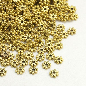May include: A large pile of gold-colored metal beads with a flower-like design. The beads are small and have a hole in the center for stringing.