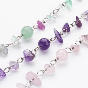 May include: A silver chain necklace with green, pink, and purple gemstone beads. The beads are various shapes and sizes, including round, oval, and irregular.