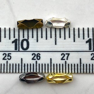 Puede incluir: Cuatro componentes de joyer&iacute;a met&aacute;licos en bronce, plata, metal de ca&ntilde;&oacute;n y oro. Cada componente es una peque&ntilde;a cuenta en forma de barril con un dise&ntilde;o ondulado. Las cuentas se colocan cerca de una regla.
