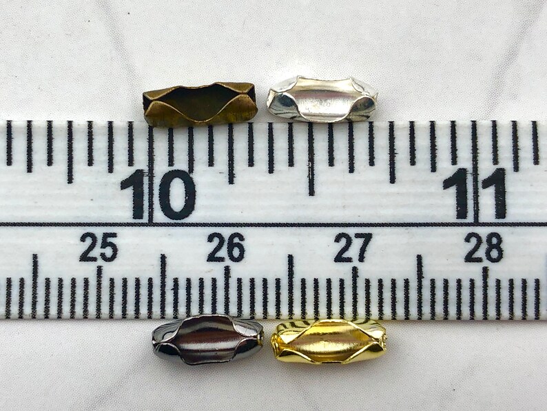 Puede incluir: Cuatro componentes de joyer&iacute;a met&aacute;licos en bronce, plata, metal de ca&ntilde;&oacute;n y oro. Cada componente es una peque&ntilde;a cuenta en forma de barril con un dise&ntilde;o ondulado. Las cuentas se colocan cerca de una regla.