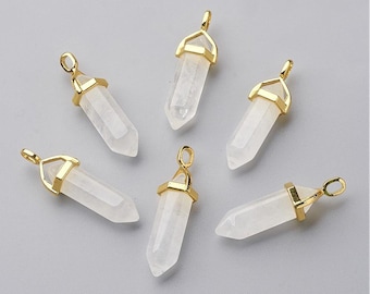 May include: Six clear quartz crystal pendants with gold-colored metal caps and loops. The crystals are hexagonal in shape and have a polished, translucent appearance. The pendants are arranged on a light gray surface.