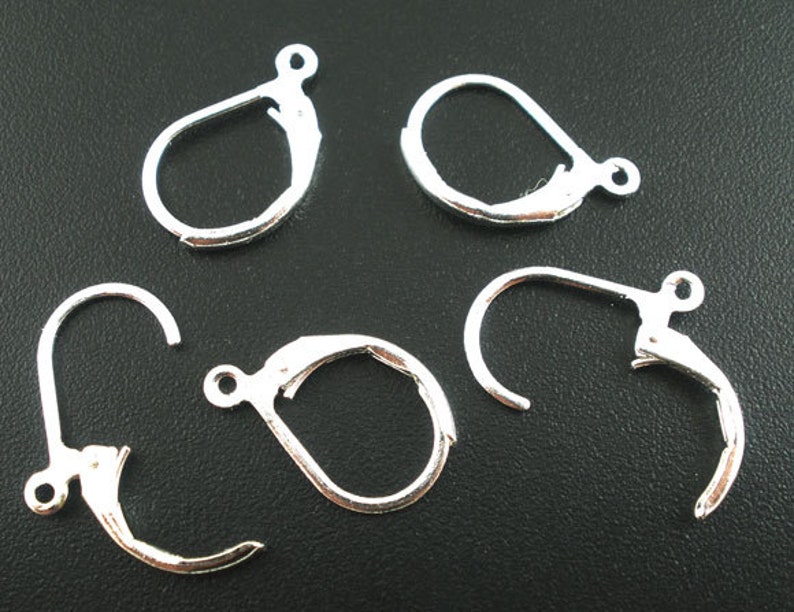 May include: Five silver earring hooks, also known as leverback earring findings, are shown on a black surface. The hooks are made of metal and have a smooth finish.