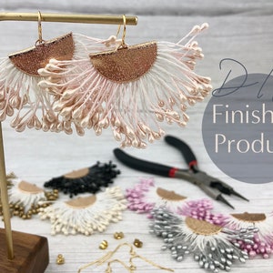 May include: DIY finished product, a pair of pink and white tassel earrings with gold accents. The earrings are displayed on a wooden stand with other earrings in various colors.