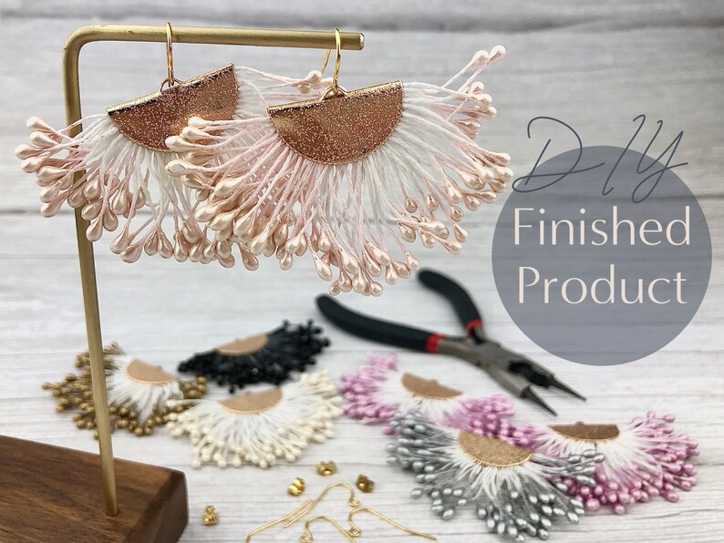 May include: DIY finished product, a pair of pink and white tassel earrings with gold accents. The earrings are displayed on a wooden stand with other earrings in various colors.