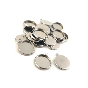 May include: A pile of silver metal round pendant trays with a loop at the top. The trays are stacked on top of each other. There are two trays in the foreground that are not stacked.