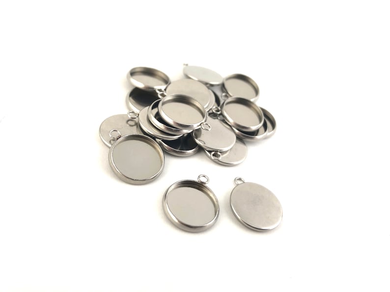 May include: A pile of silver metal round pendant trays with a loop at the top. The trays are stacked on top of each other. There are two trays in the foreground that are not stacked.