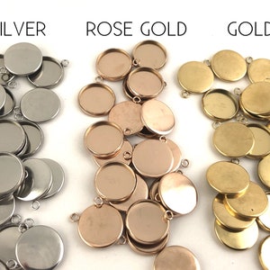 May include: A collection of round metal pendant trays in silver, rose gold, and gold. The trays are designed to hold small items, such as photos, charms, or other decorative elements.