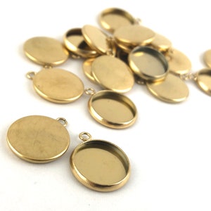 May include: A group of gold-toned metal round pendant trays with a smooth, shiny finish. The trays have a lip around the edge and a small loop at the top for attaching to a chain or cord.