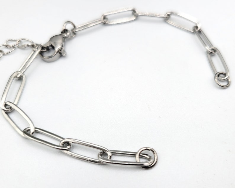 Pu&ograve; includere: Un braccialetto a catena d'argento con chiusura a moschettone. La catena &egrave; composta da maglie ovali.
