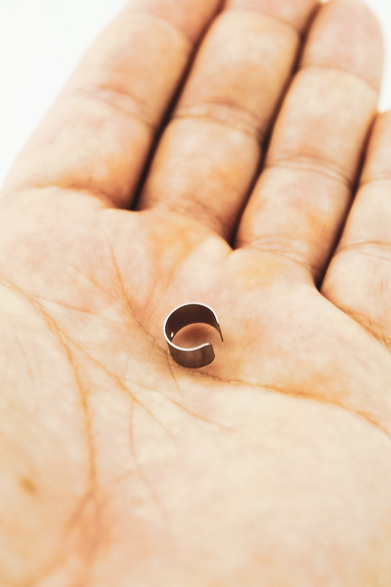 May include: A silver metal ring with a rounded shape, lying on a person's palm.