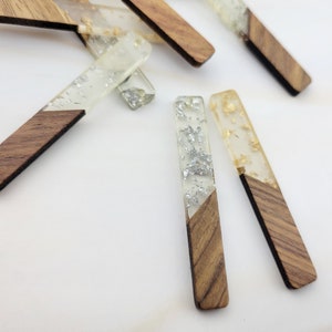 May include: A set of six wooden and clear resin bookmarks. Each bookmark is a rectangular shape with a wood base and a clear resin top. The resin is filled with silver or gold glitter.