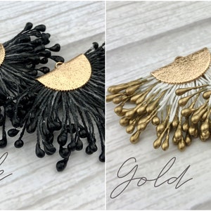 May include: A pair of dangle earrings with a gold half-circle base and black or gold teardrop-shaped beads. The earrings are shown against a white wood background. "Black" and "Gold" are written below the earrings.
