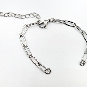 Pu&ograve; includere: Un braccialetto a catena d'argento con chiusura a moschettone. La catena &egrave; composta da maglie ovali.