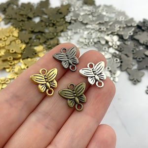 May include: Assortment of metal butterfly charms in gold, silver, and antique brass finishes. Each charm features a detailed butterfly design with two jump rings for attaching to jewelry or crafts.